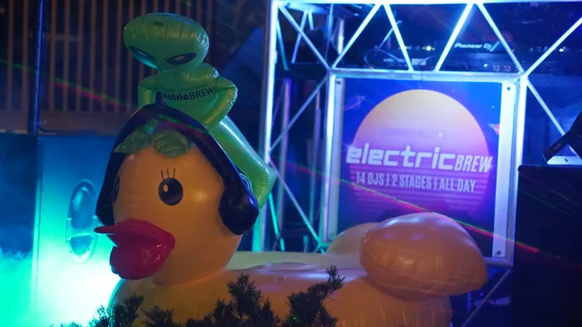 Inflatable aliens beside the glowing Electric Brew DJ booth at night